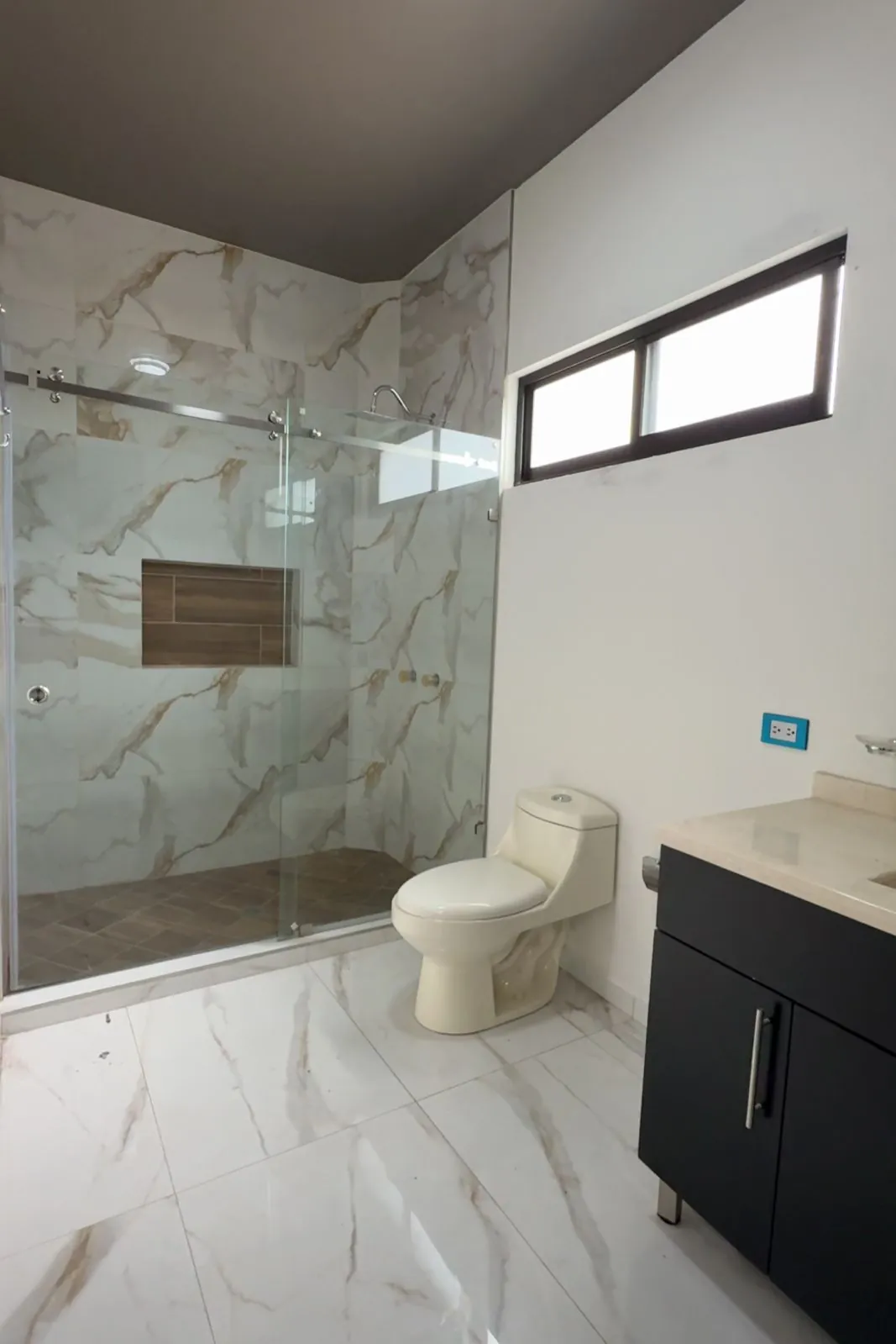 Baño completo de la recámara de planta baja con muros tipo mármol y cancel de cristal, Santa Bárbara Residencial