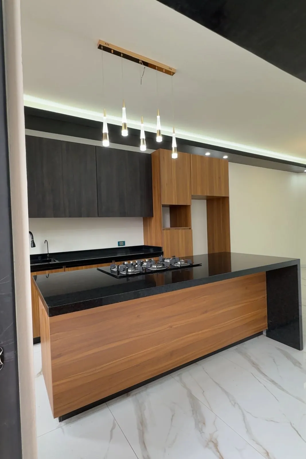 Cocina con isla de granito negro, carpintería de madera y lámparas colgantes, Santa Bárbara Residencial
