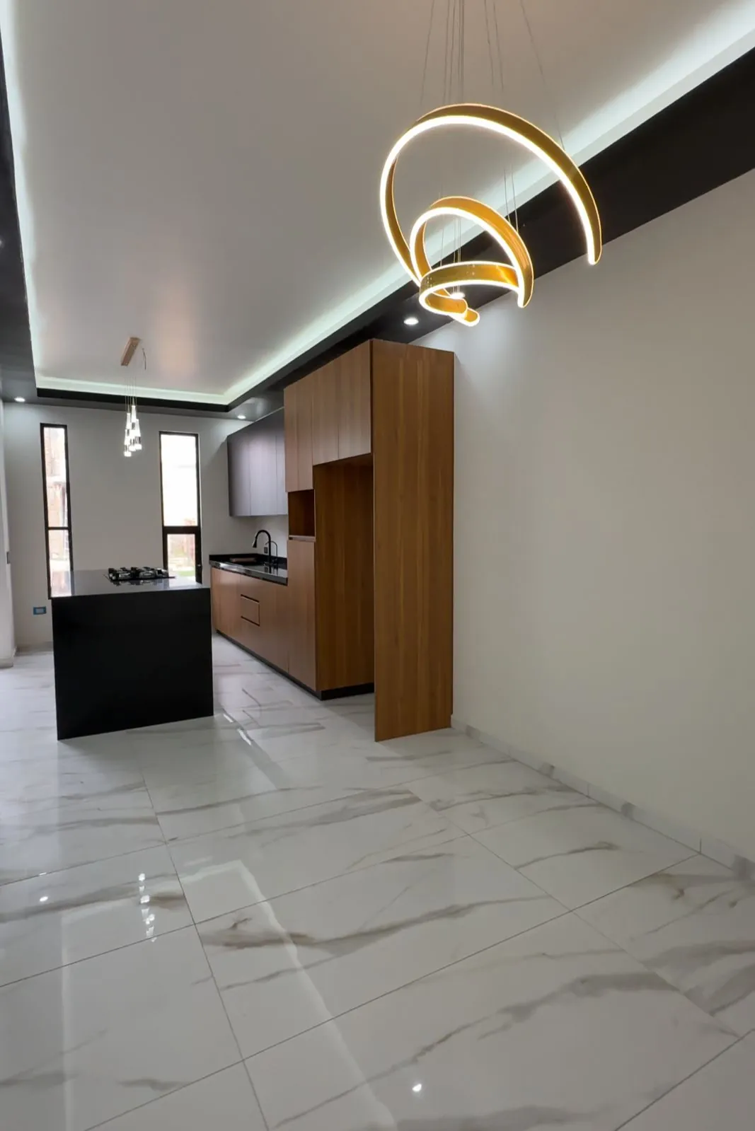 Comedor con lámpara de anillos dorados y cocina al fondo, Santa Bárbara Residencial