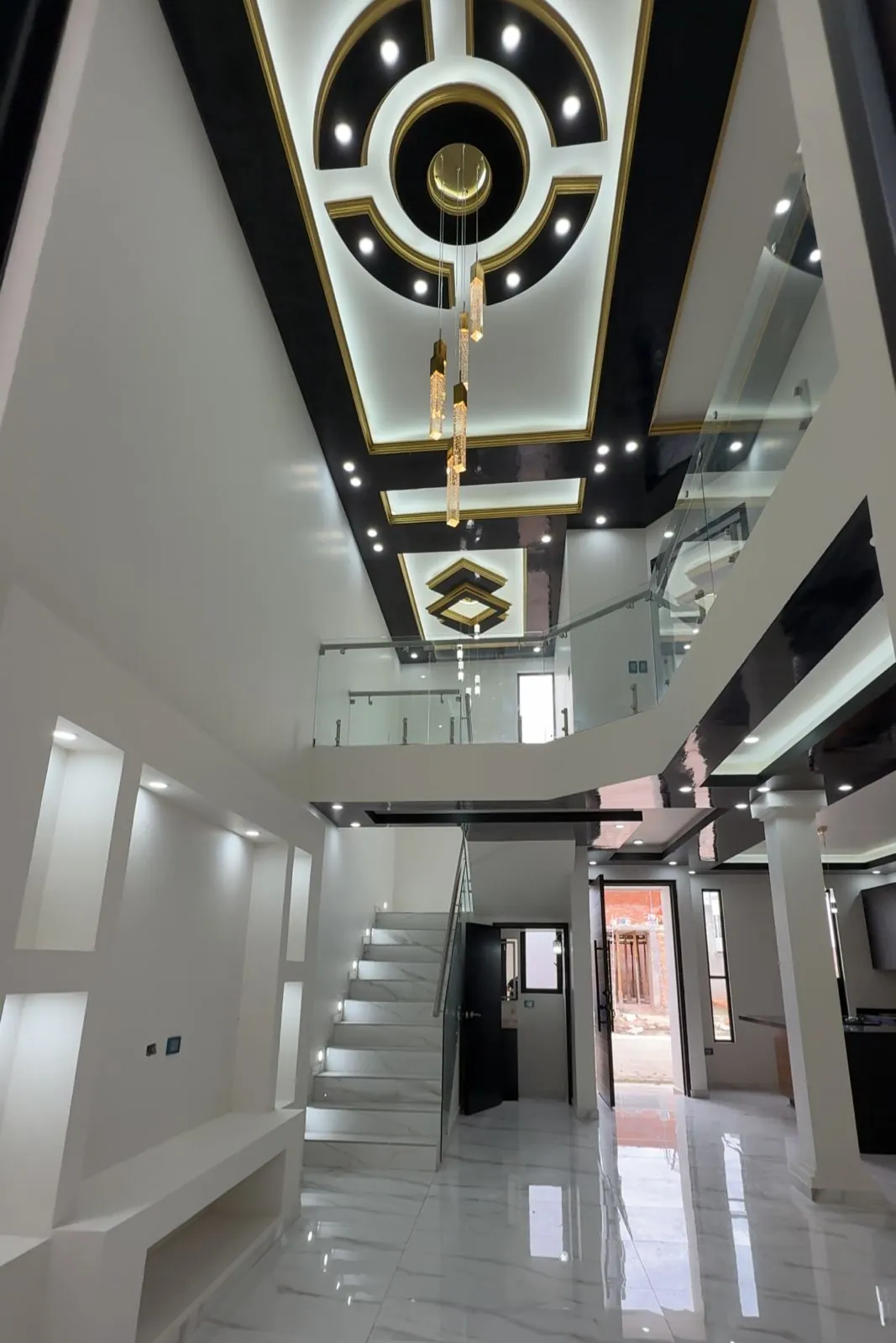 Vestíbulo a doble altura con plafón de hoja de paladio y escalera iluminada, Santa Bárbara Residencial